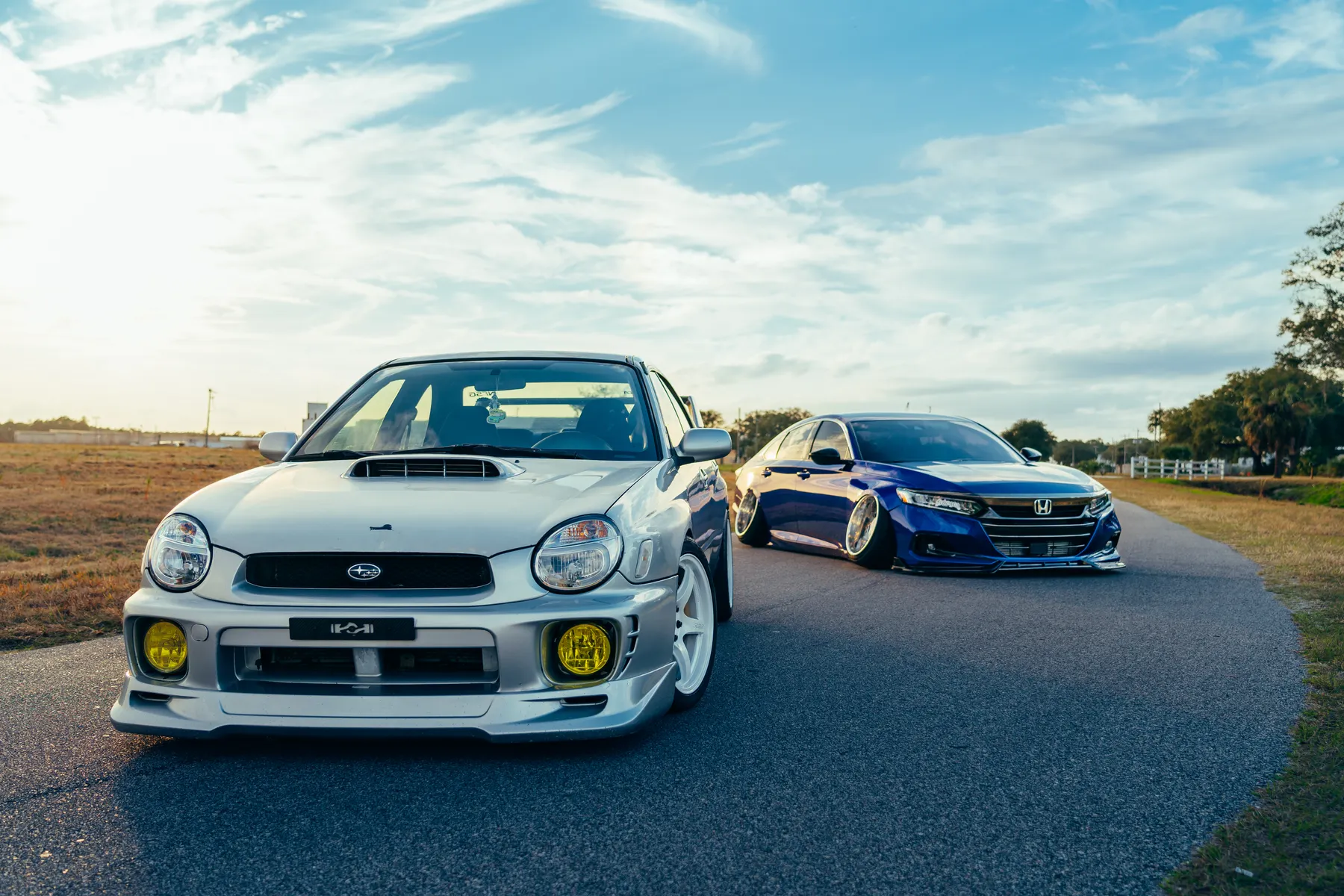 Modified performance cars parked on a scenic road at sunset